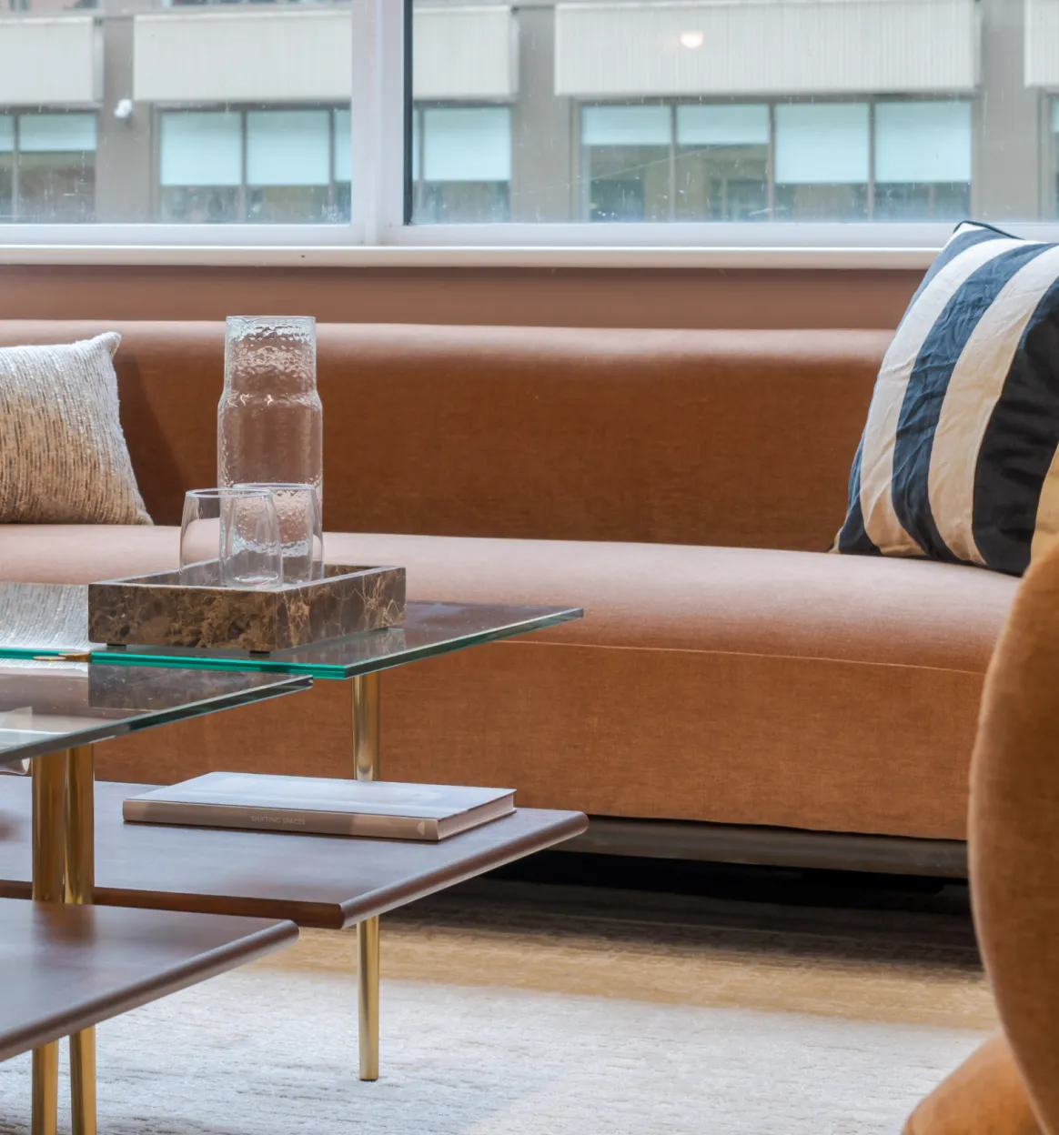 Cushions on a tan velvet sofa beside a glass carafe on a marble tray